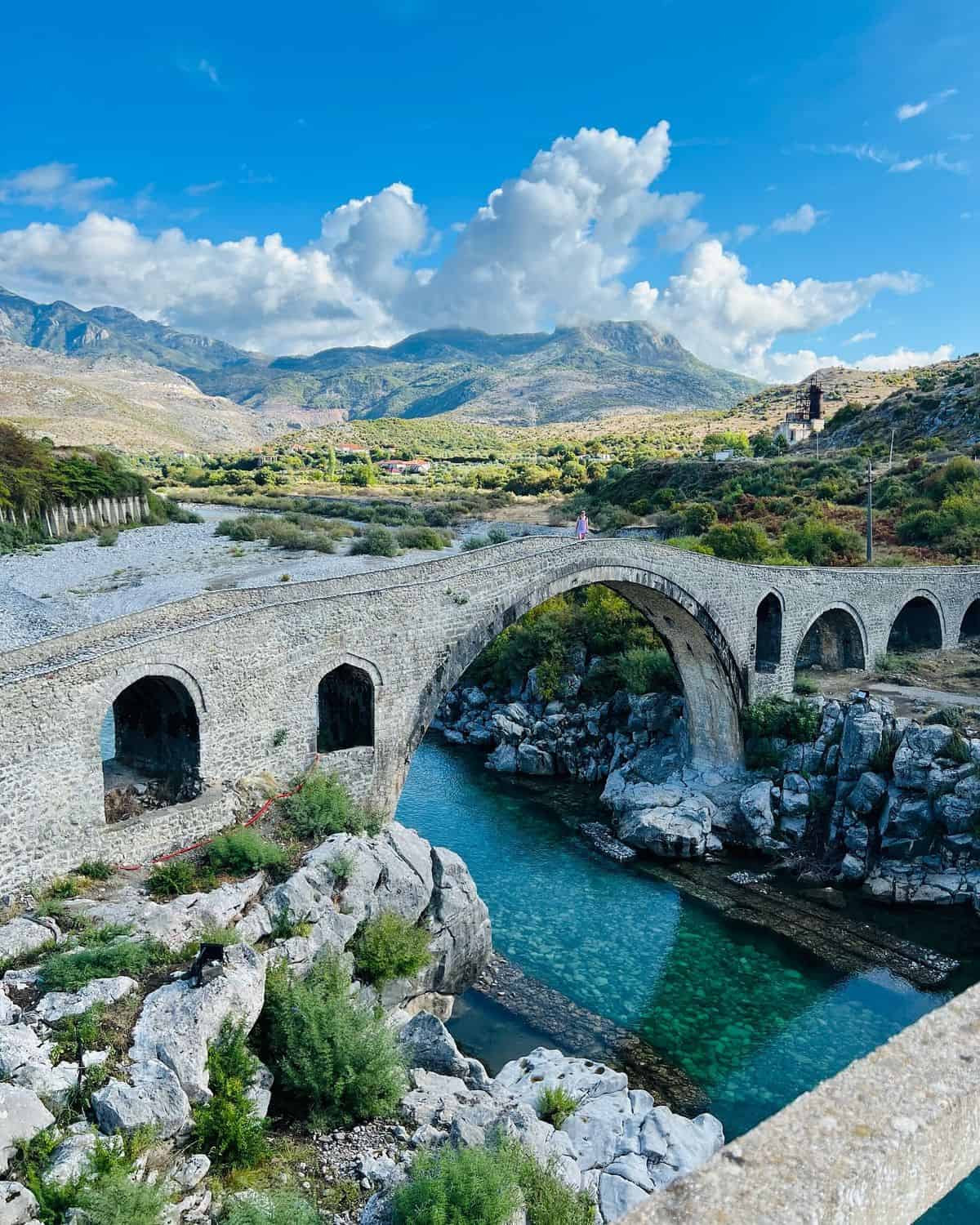 Serene mountain landscape with an ancient stone bridge over turquoise river, ideal for scenic travel and outdoor recreation.