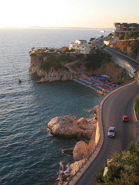 Breathtaking coastal view with rocky shoreline, modern homes, and winding road by the sea in Albania.