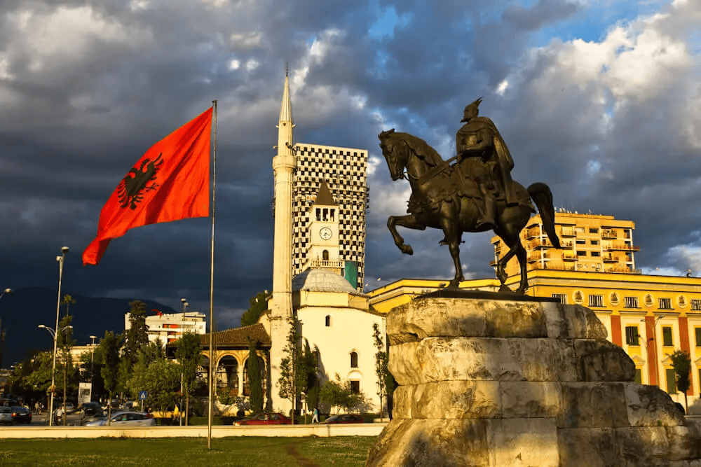 Albanian flag and historic monument in Tirana, Albania, symbolizing culture and heritage.