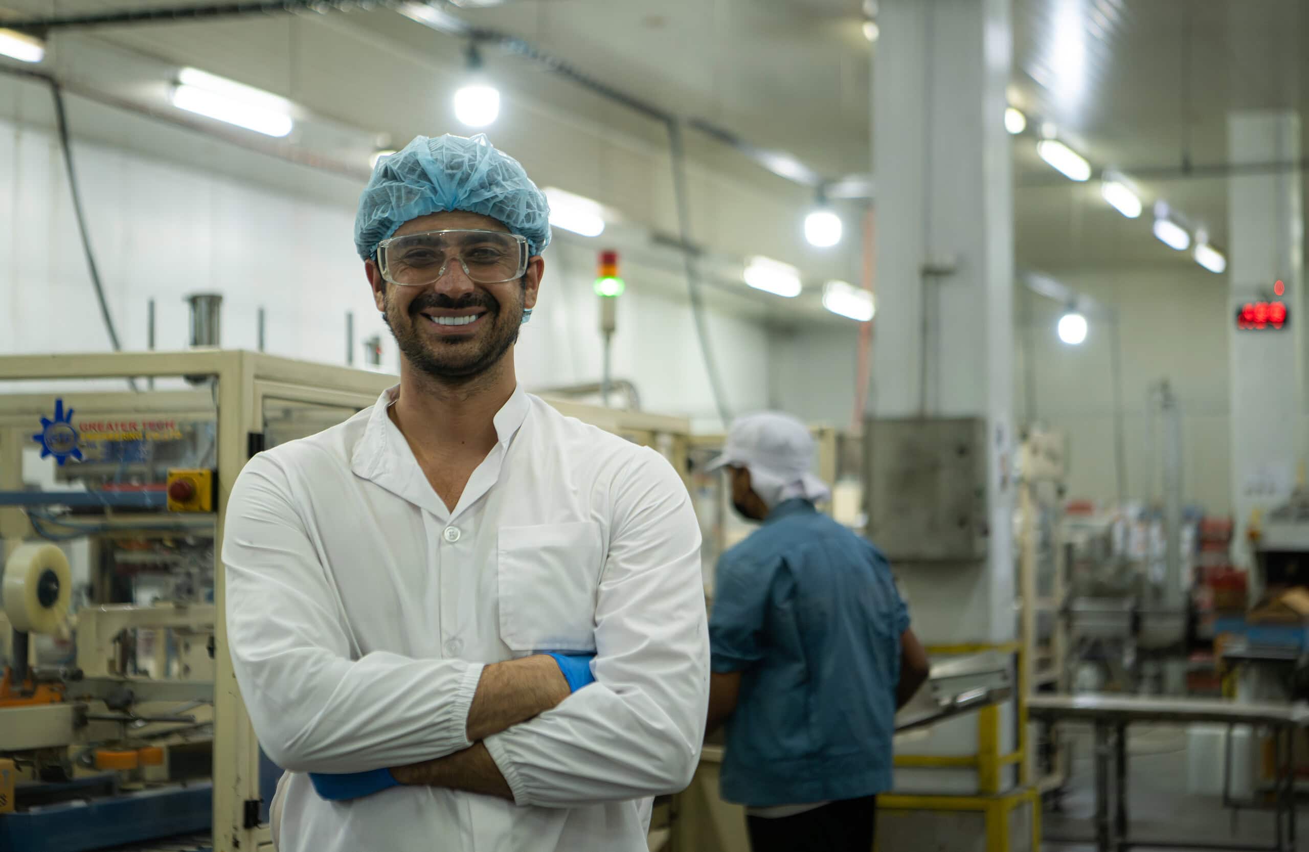 Alt: Egyptian worker smiling in industrial factory setting with safety gear.
