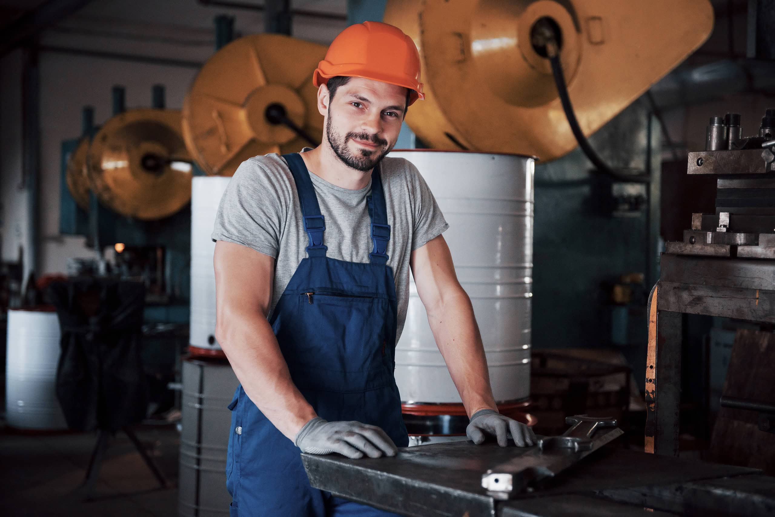Punëtor ndërtimi me kapelë të fortë në punishte industriale, duke theksuar zanatet e kualifikuara dhe shërbimet e rekrutimit.