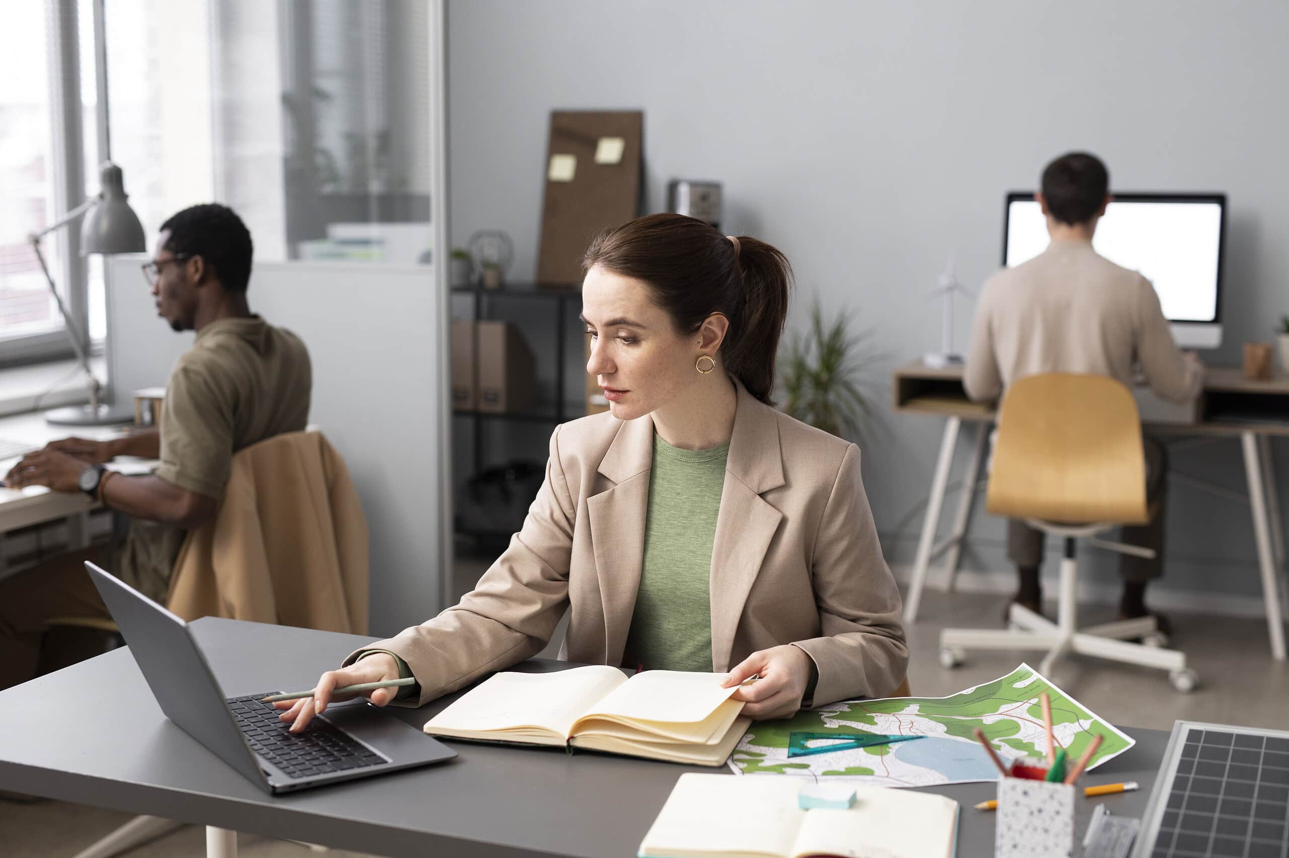 Efficient woman working on laptop and documents in modern office environment.